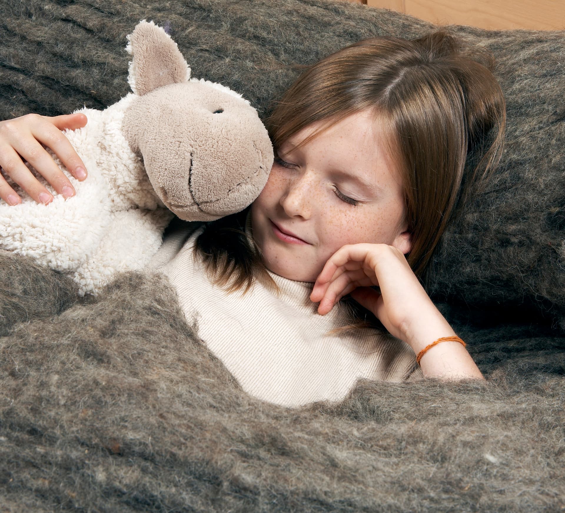 Criança a descansar confortavelmente com uma ovelha de peluche entre mantas de lã